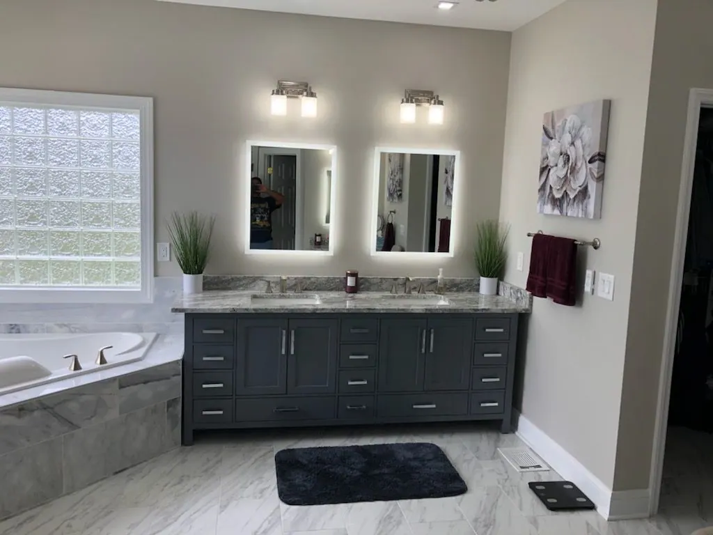 Remodeled bathroom with a double vanity, lighted mirrors and a corner tub