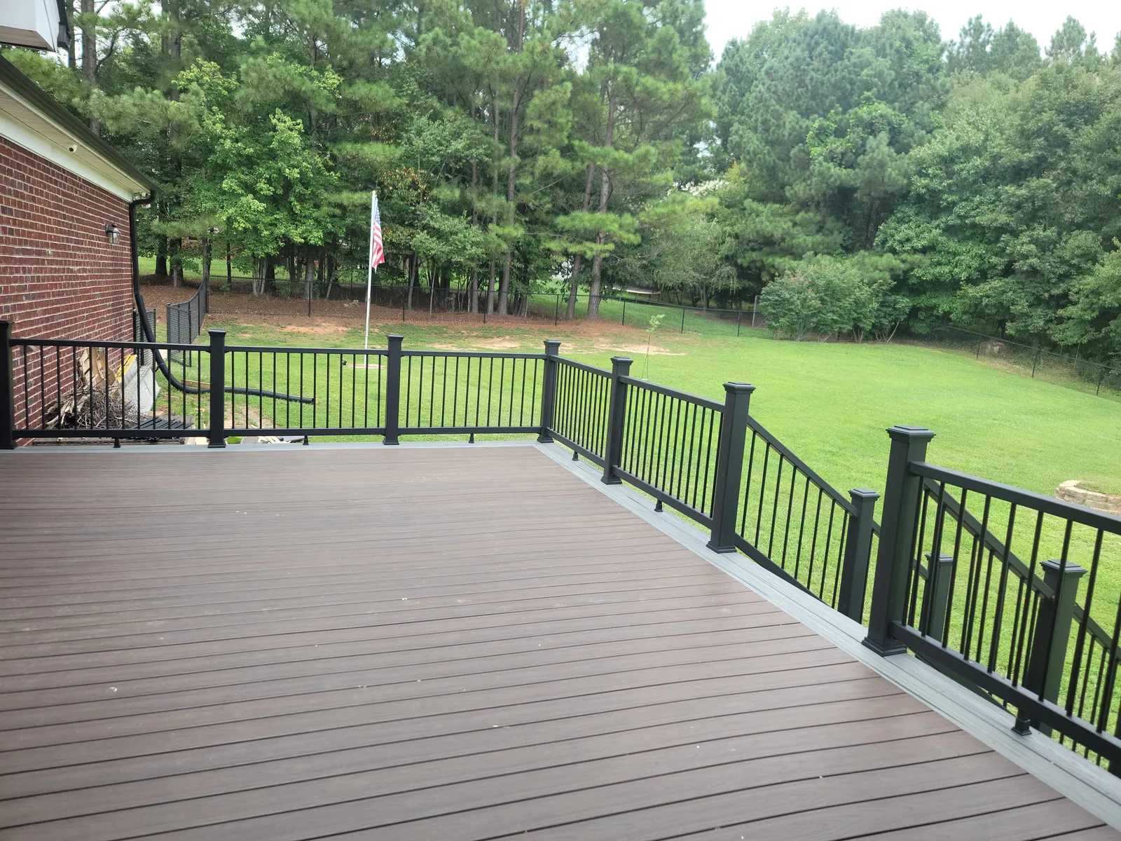 Composite deck boards with black aluminum railing overlooking a backyard