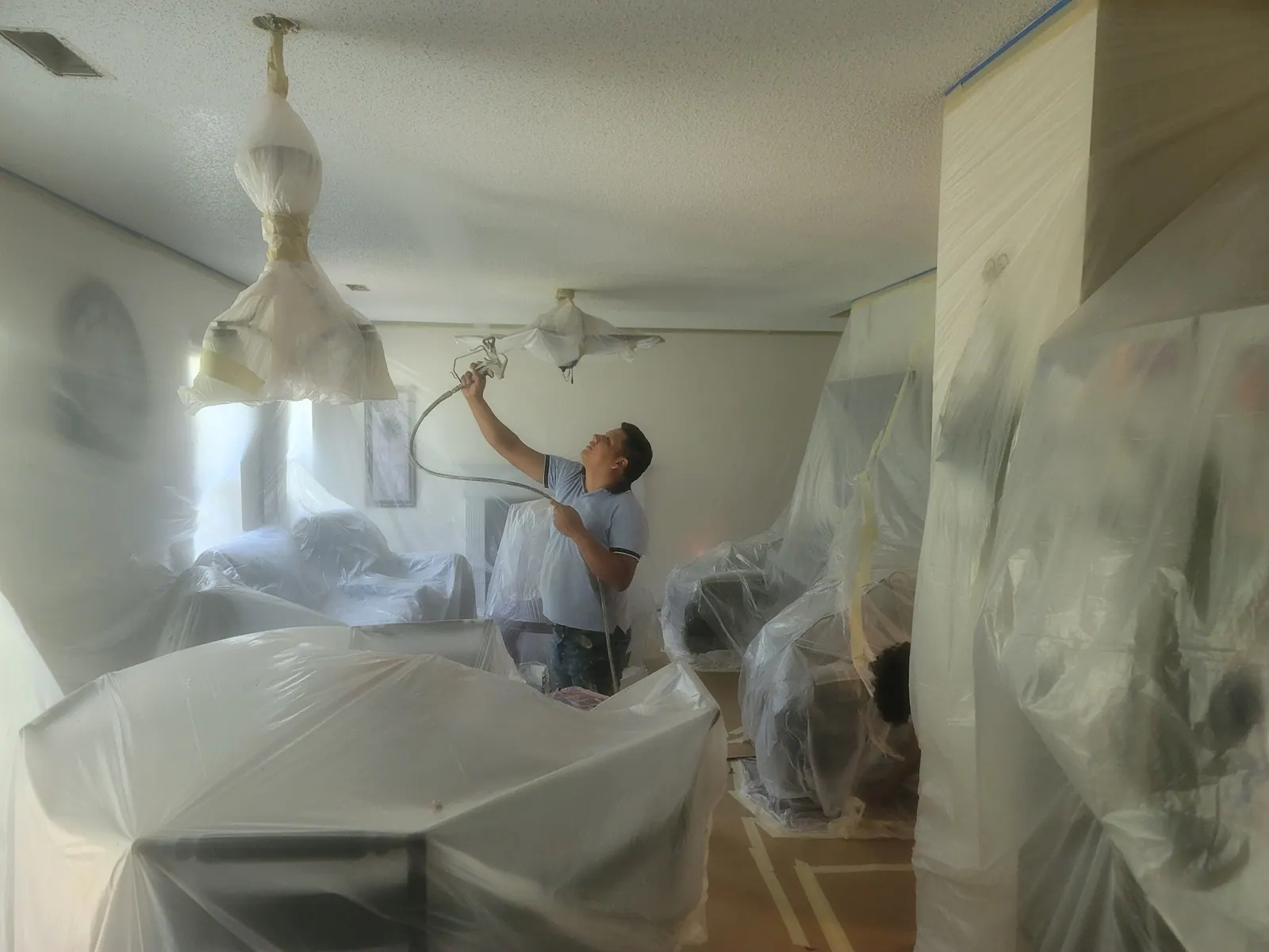 Painter spraying a ceiling in a room masked with plastic sheeting
