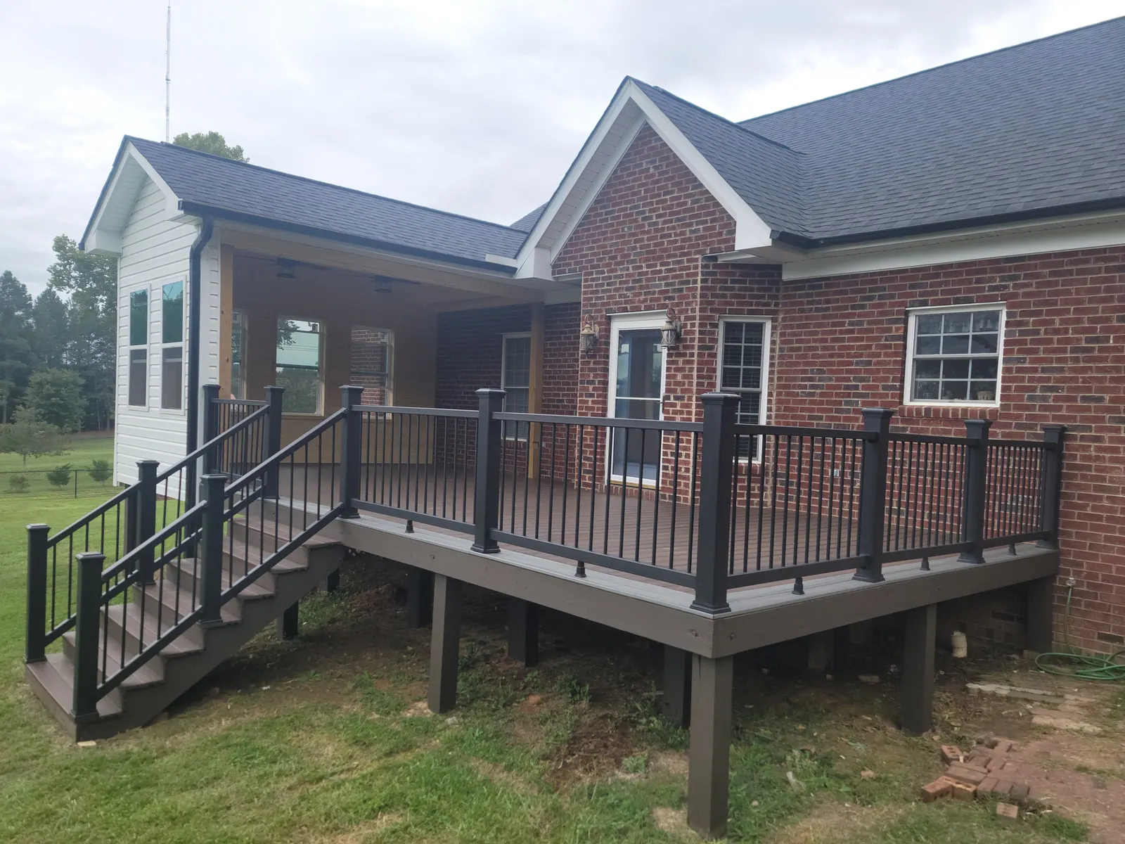 New deck with black railing and stairs beside a covered porch on a brick home