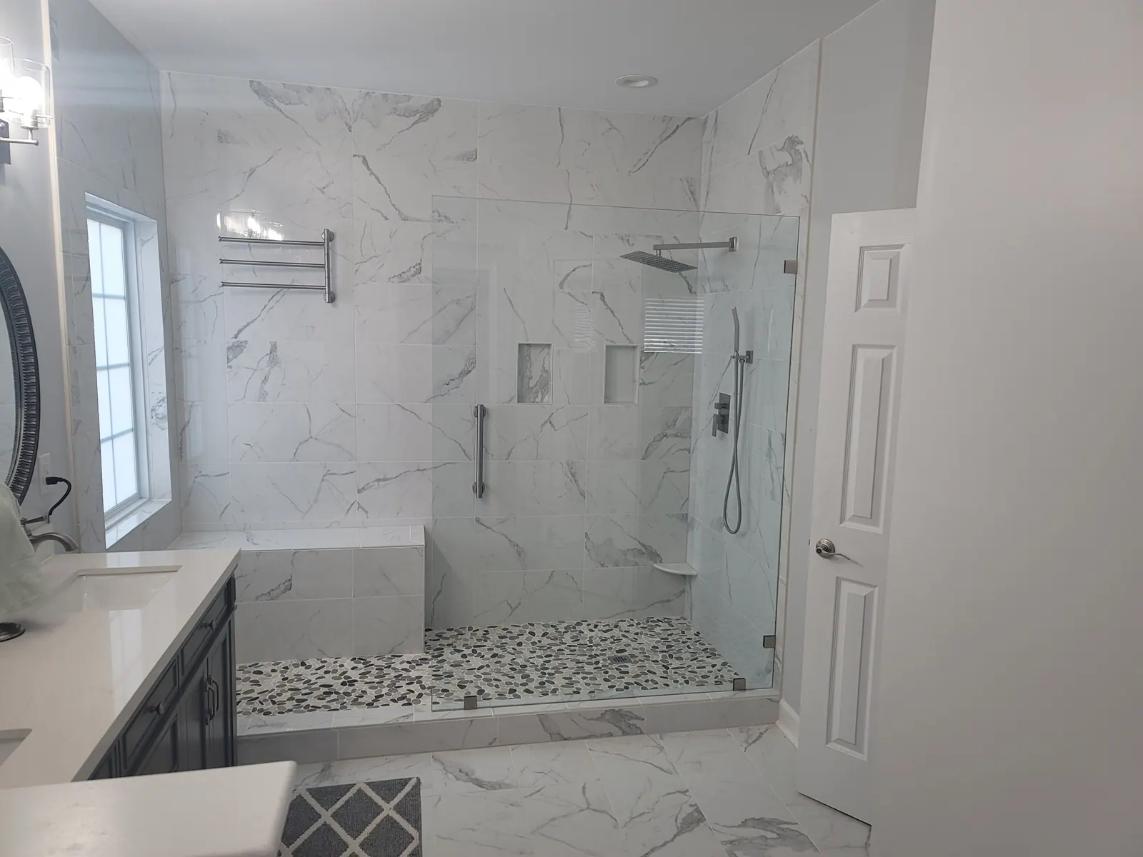 Walk-in shower with marble-look walls, a bench and a glass panel